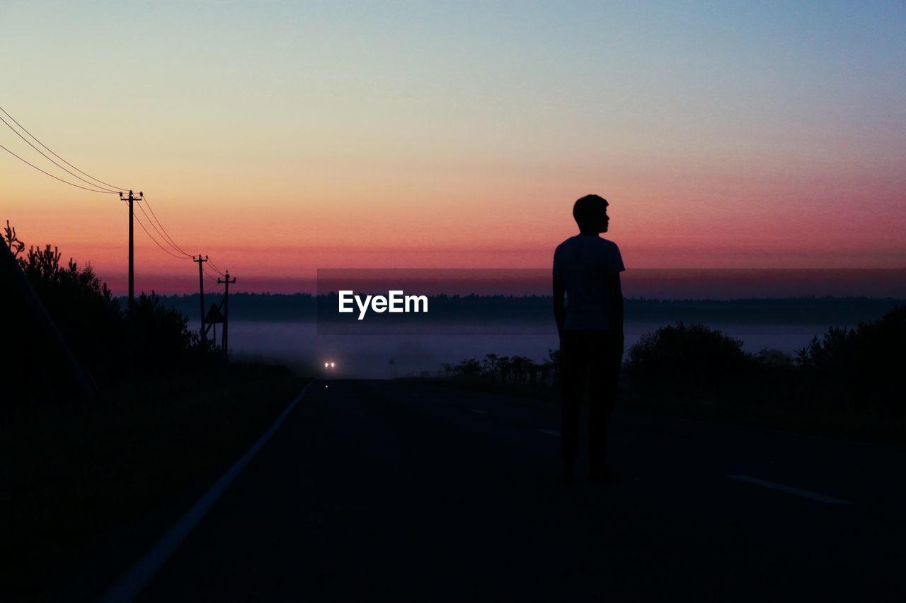 Silhouette man standing on road against sky during sunset