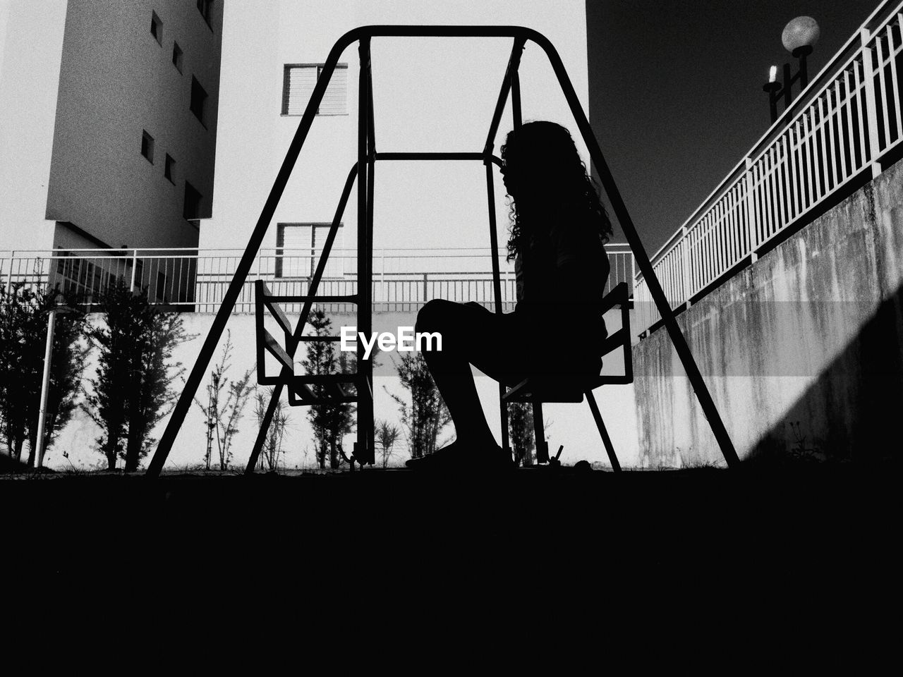 Silhouette woman sitting on seat at playground