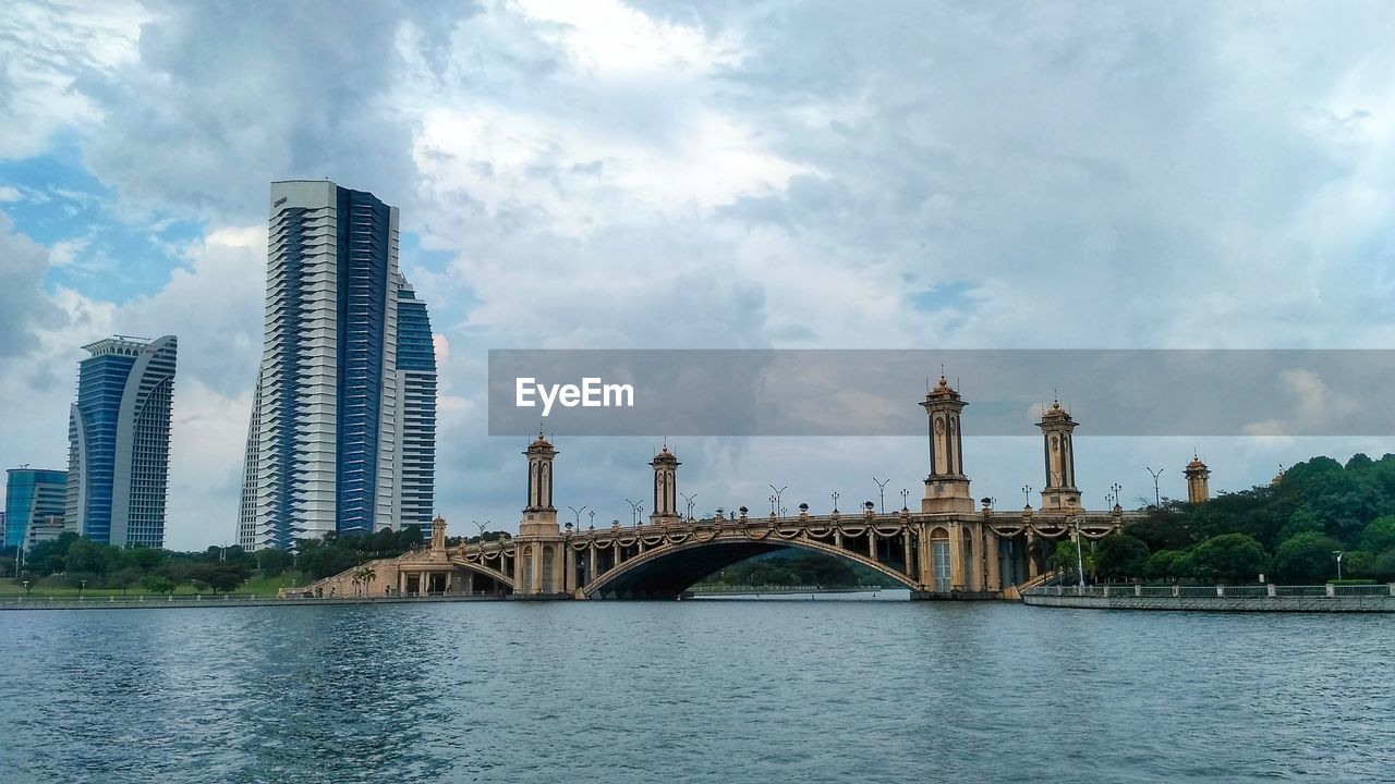 Bridge over river by buildings against sky