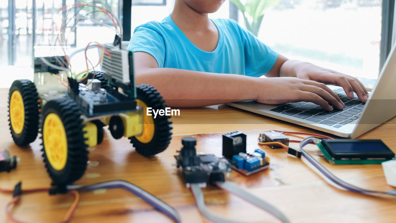 Midsection of boy using laptop by toy on table