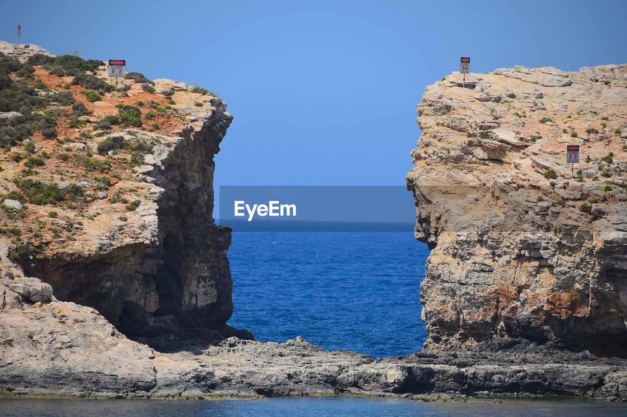 Scenic view of sea and rocks against clear blue sky