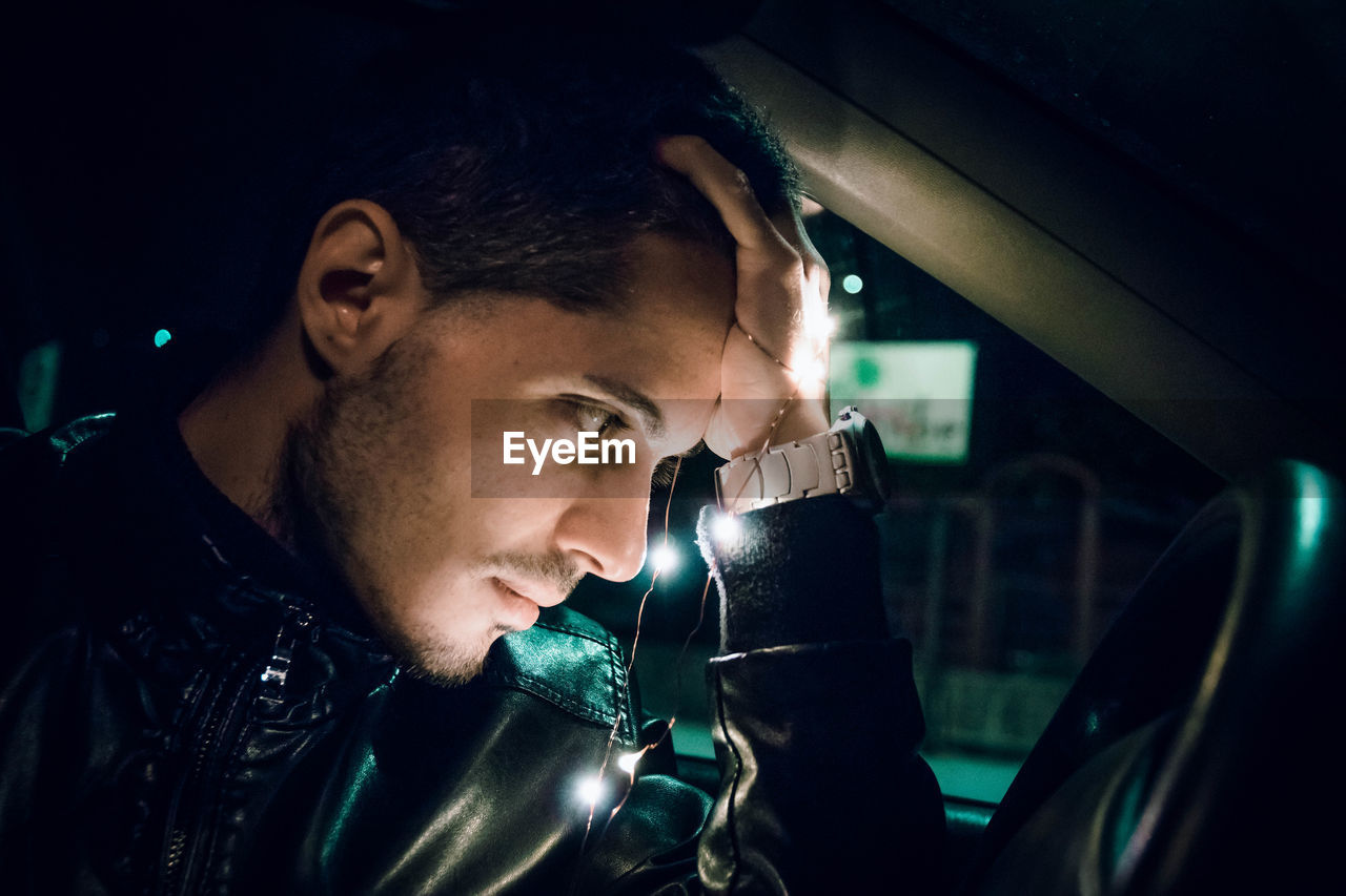 Young man with illuminated string light sitting in car at night