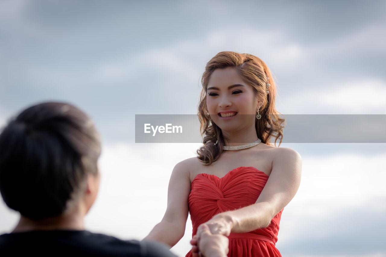 REAR VIEW OF WOMAN SMILING AGAINST SKY