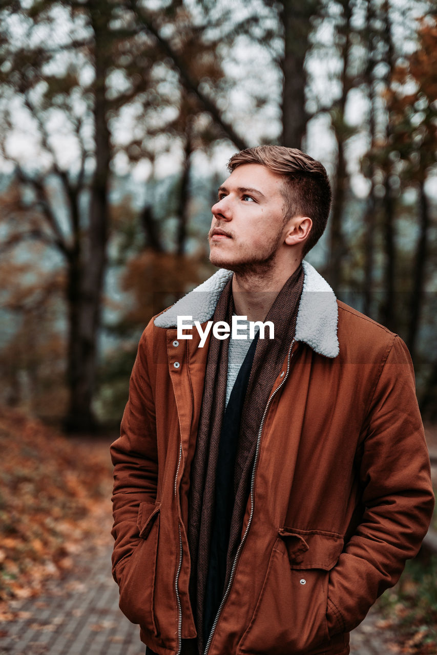 Young man looking away while standing in park