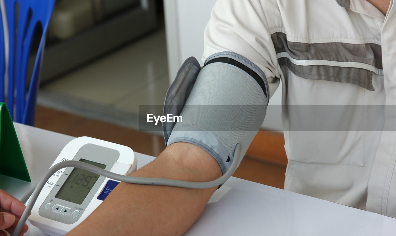 Midsection of patient examining blood pressure on table in hospital