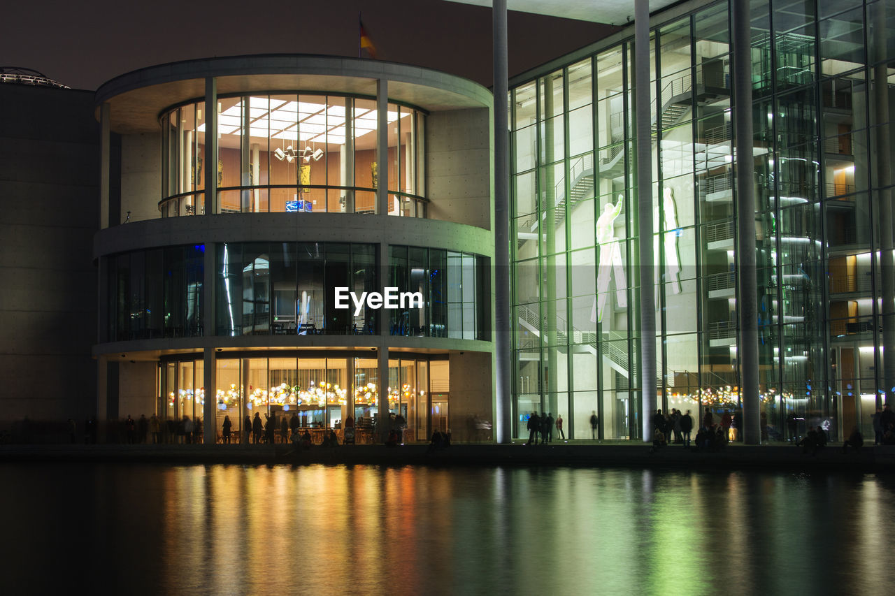 Silhouette people in illuminated glass building at night