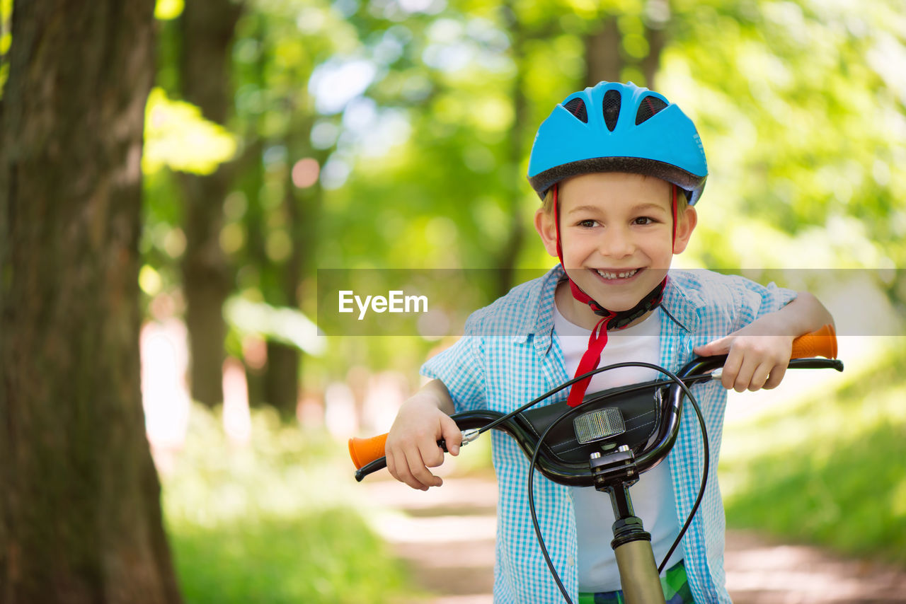 Portrait of smiling boy wearing helmet standing with bicycle at park