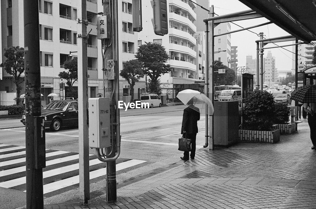 FULL LENGTH OF MAN WALKING ON STREET BY BUILDINGS