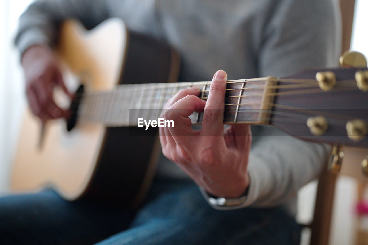 Midsection of man playing acoustic guitar