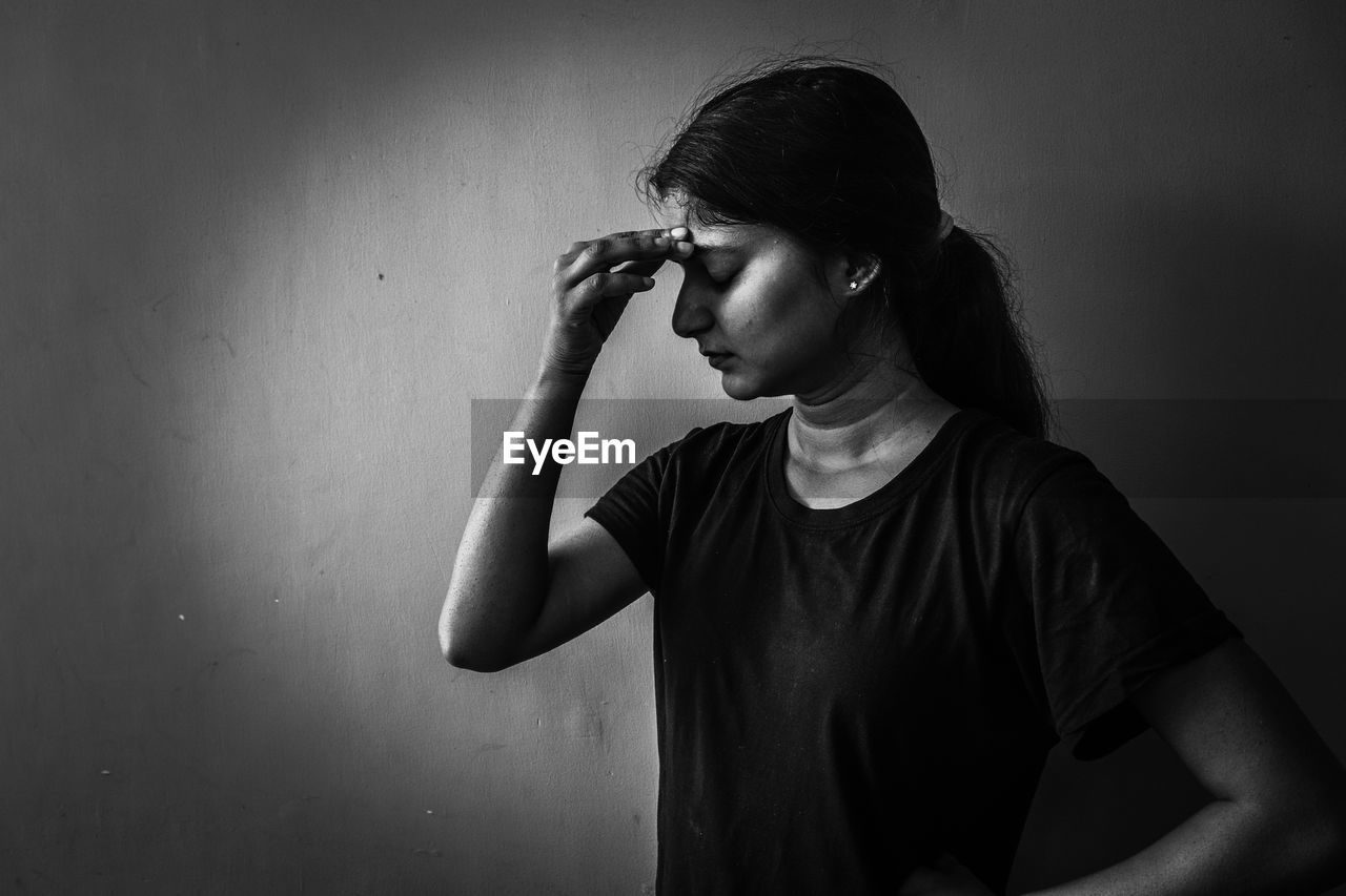 Depressed woman standing by wall at home