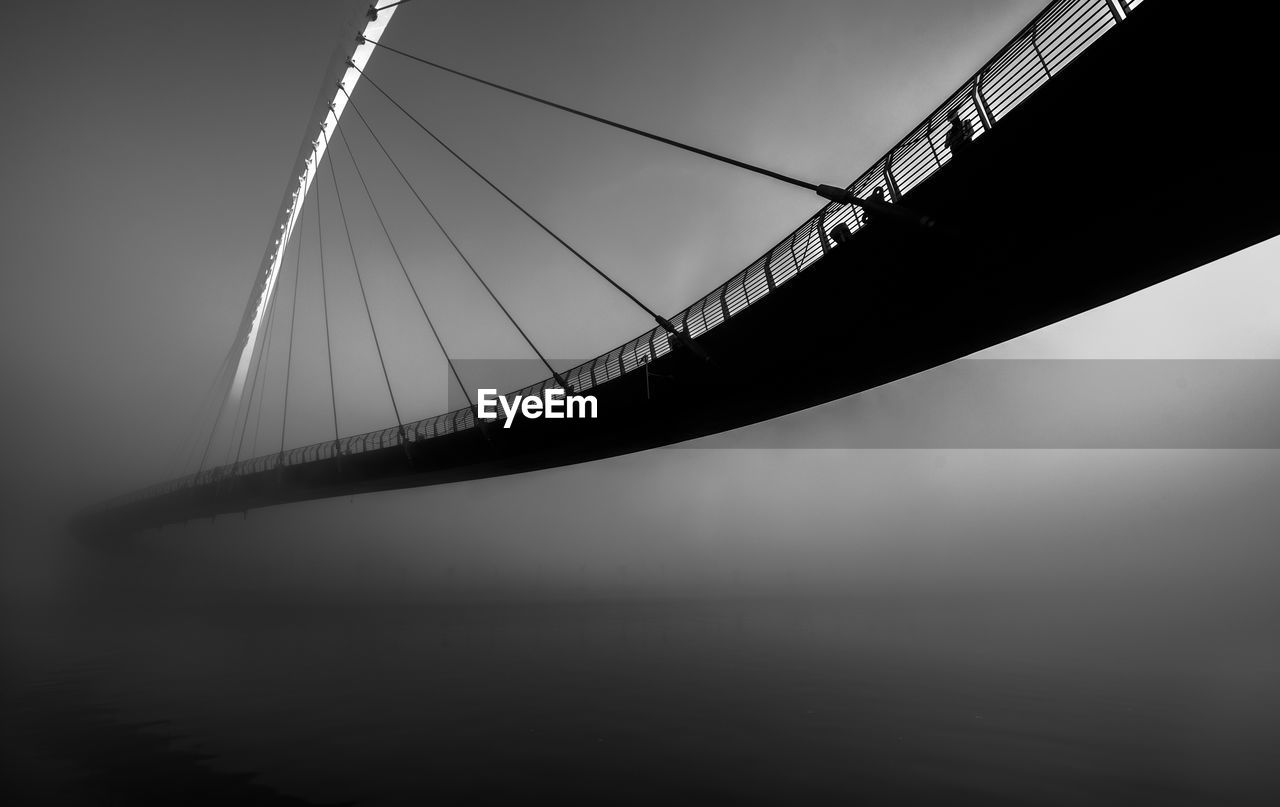 LOW ANGLE VIEW OF SUSPENSION BRIDGE AGAINST SKY IN CITY