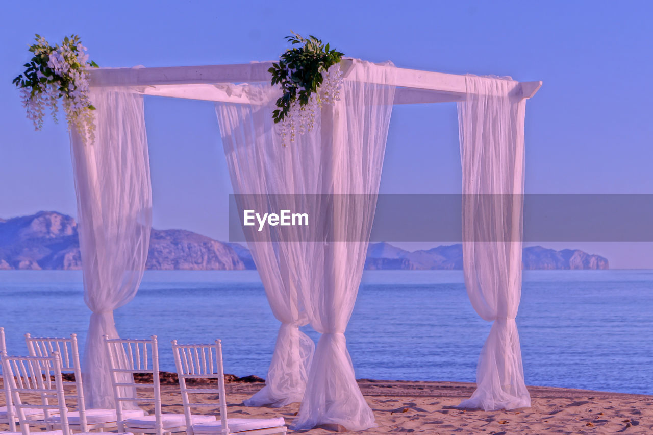 Chairs under baldachine on beach against clear sky