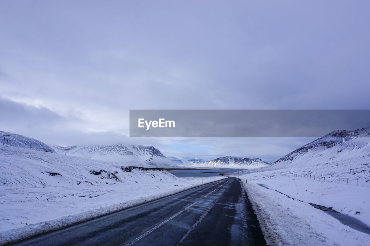 Road leading towards snow covered landscape against sky