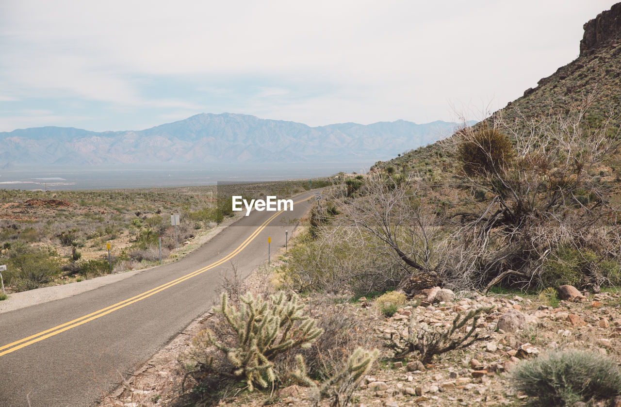 Empty country road passing through arid landscape against sky