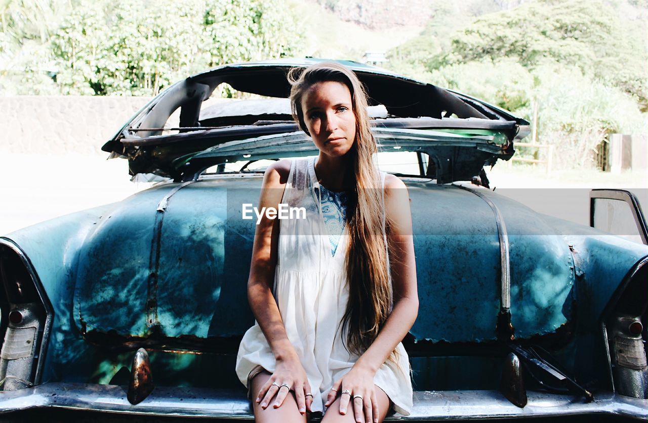 Close-up portrait of woman sitting on abandoned car