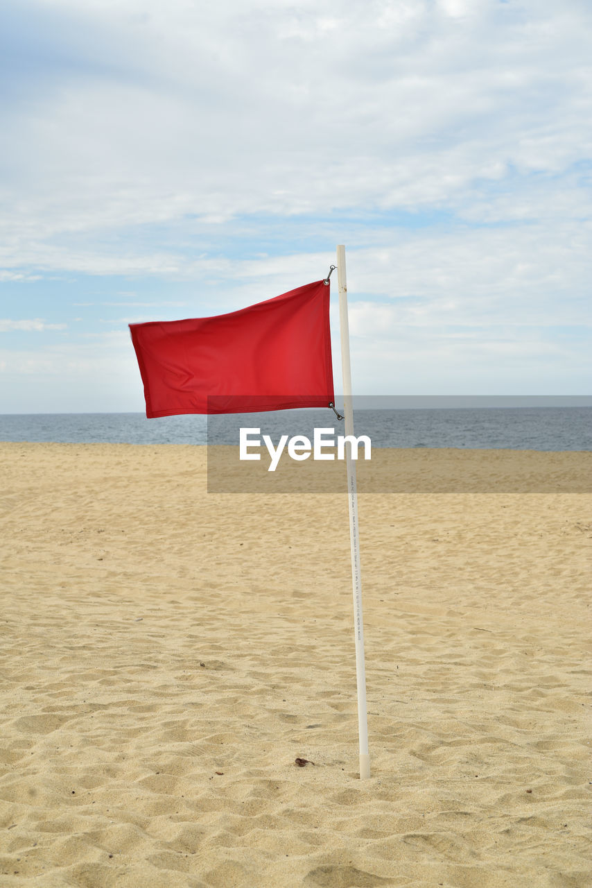 Red flag blowing in wind of seashore