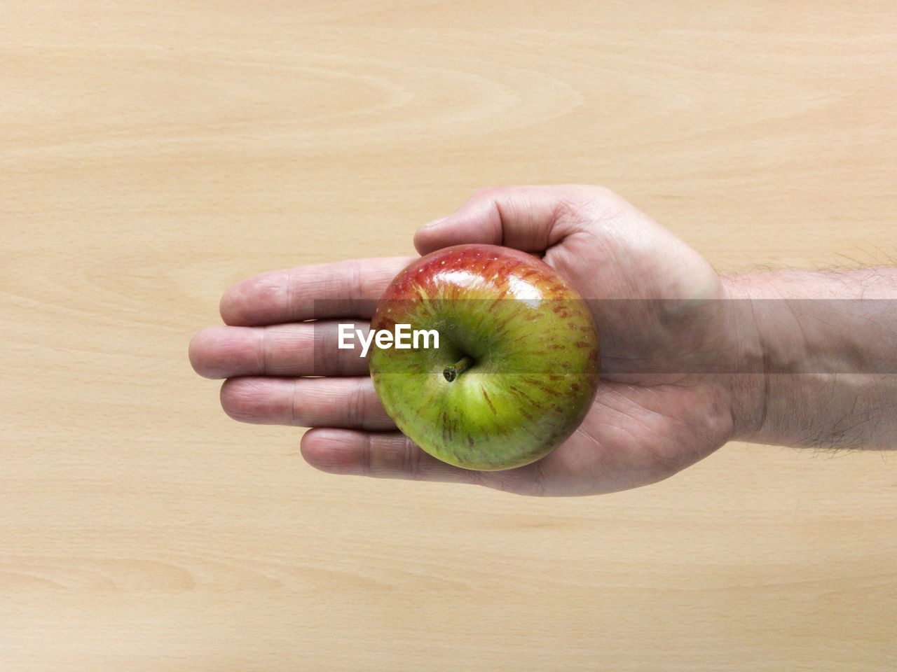 Cropped hand holding apple against table 