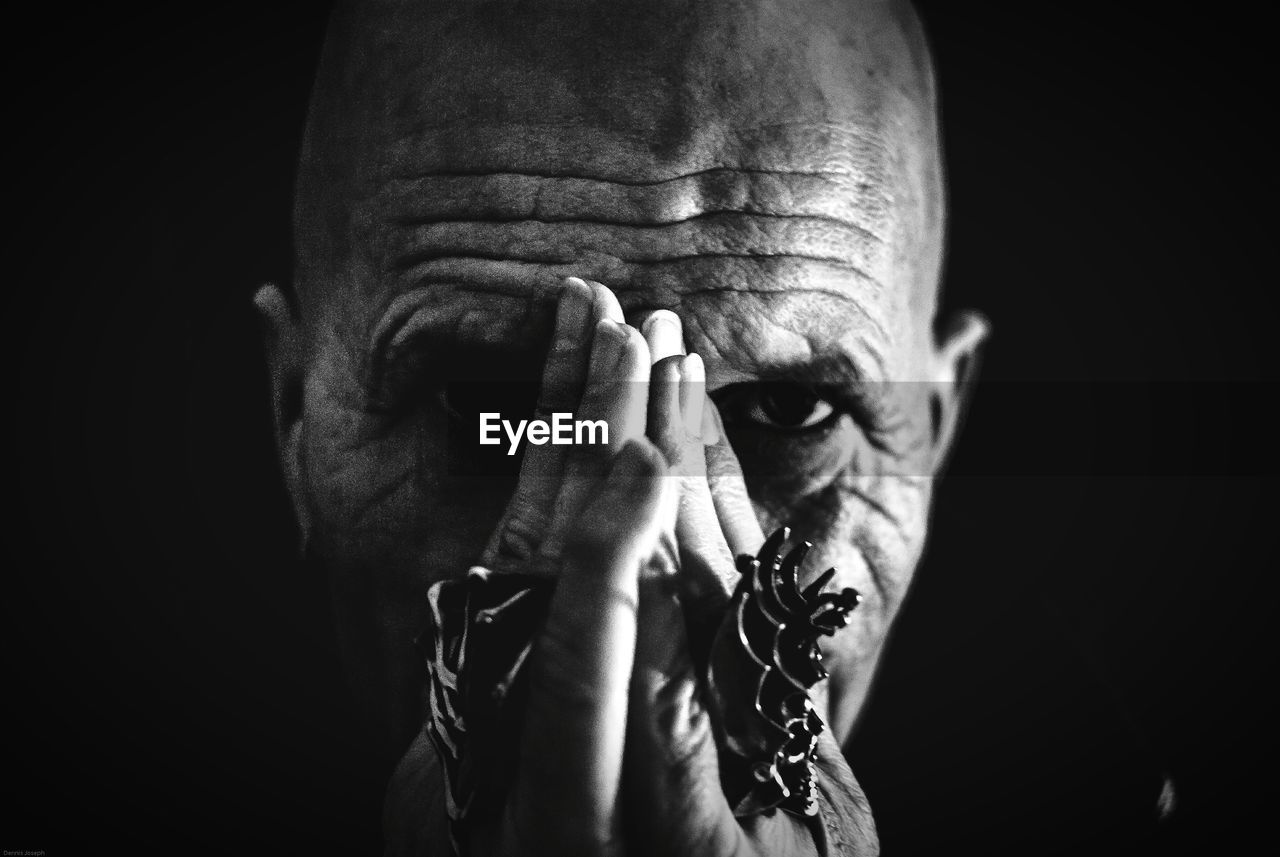 Portrait of mature man covering face with hands against black background