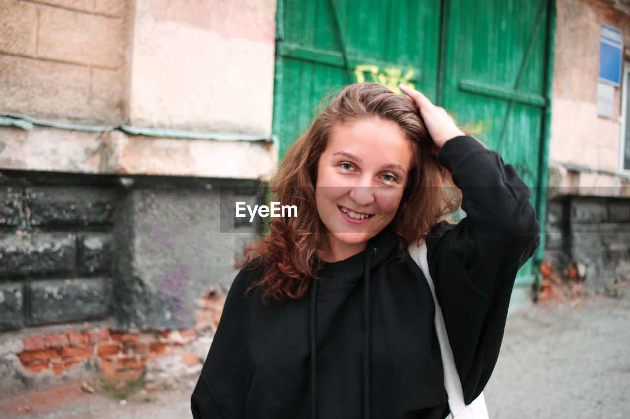 Happy young woman in black hoodie on building background