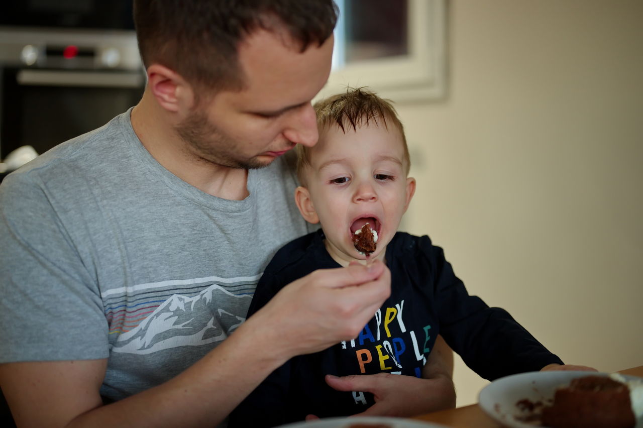 Father feeding his little toddler with chocolate cake