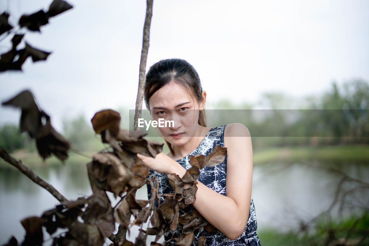 Young woman looking away while standing by plants against lake