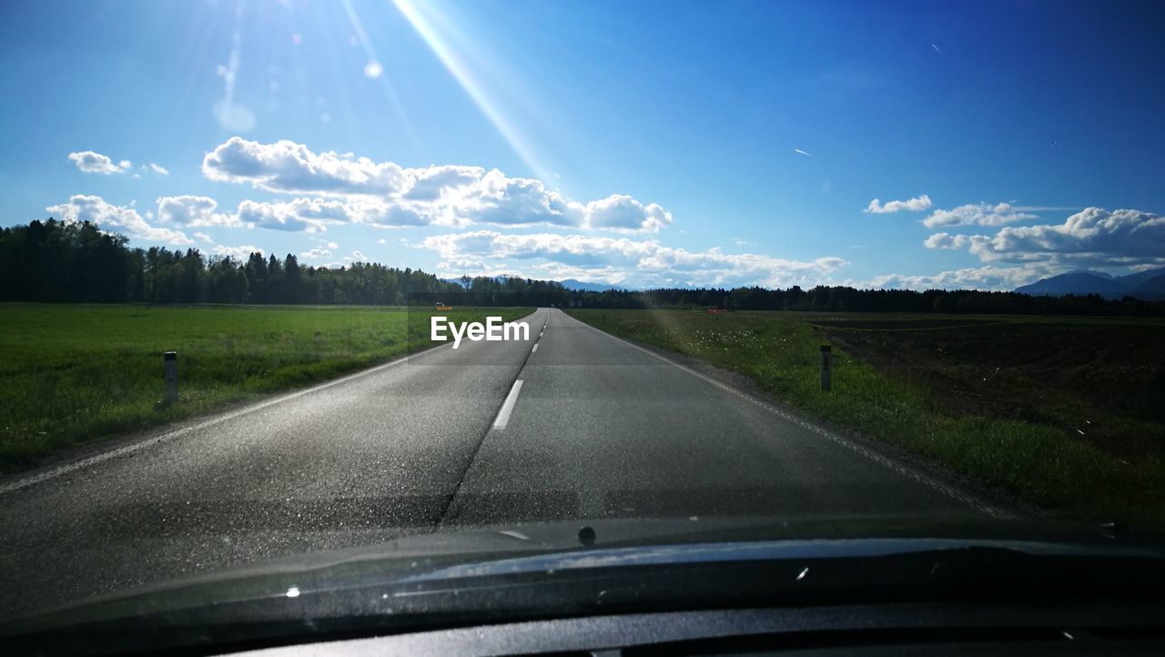 Road amidst trees against sky seen through car windshield