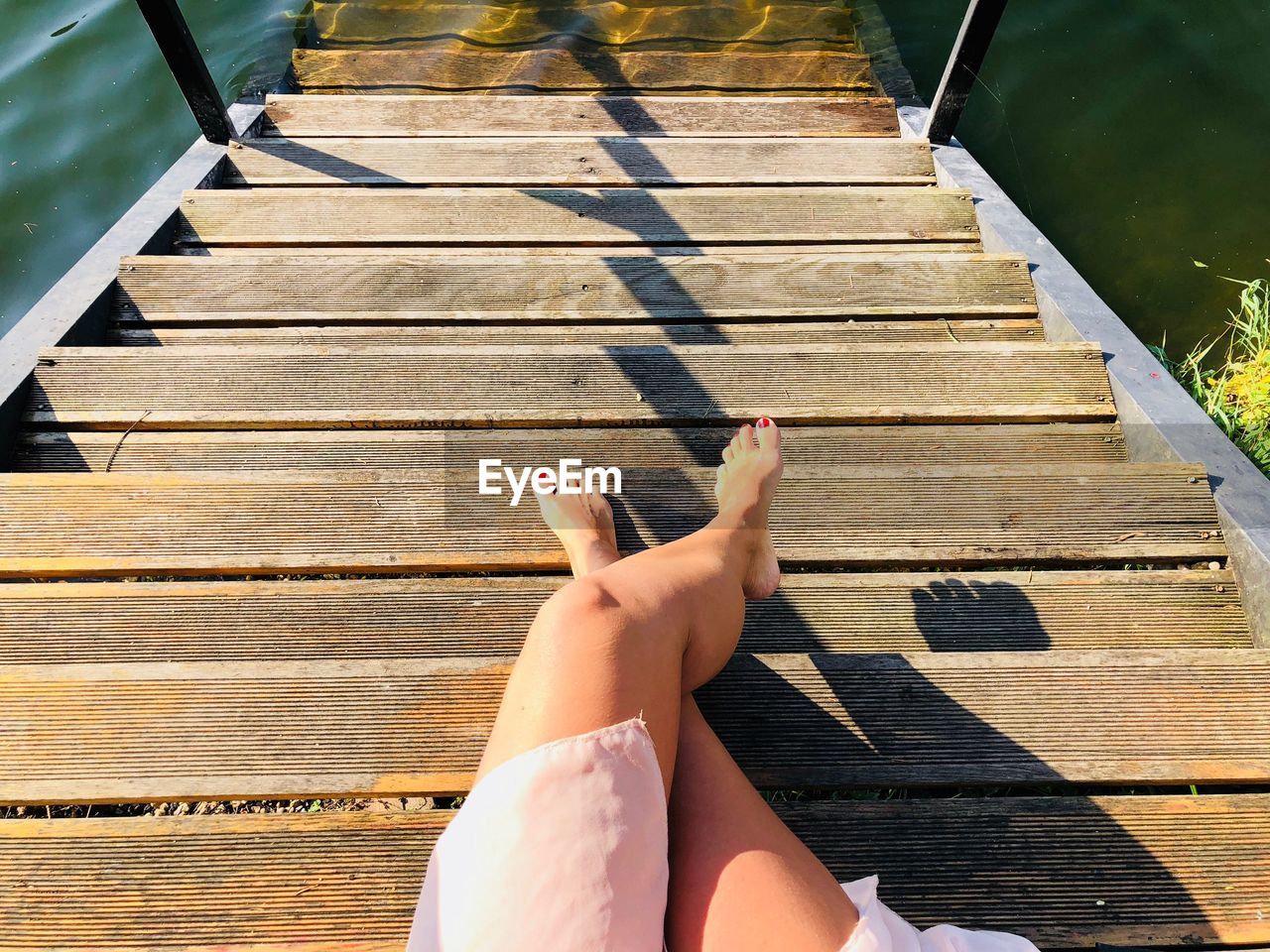 Low section of woman sitting on wooden steps leading towards lake