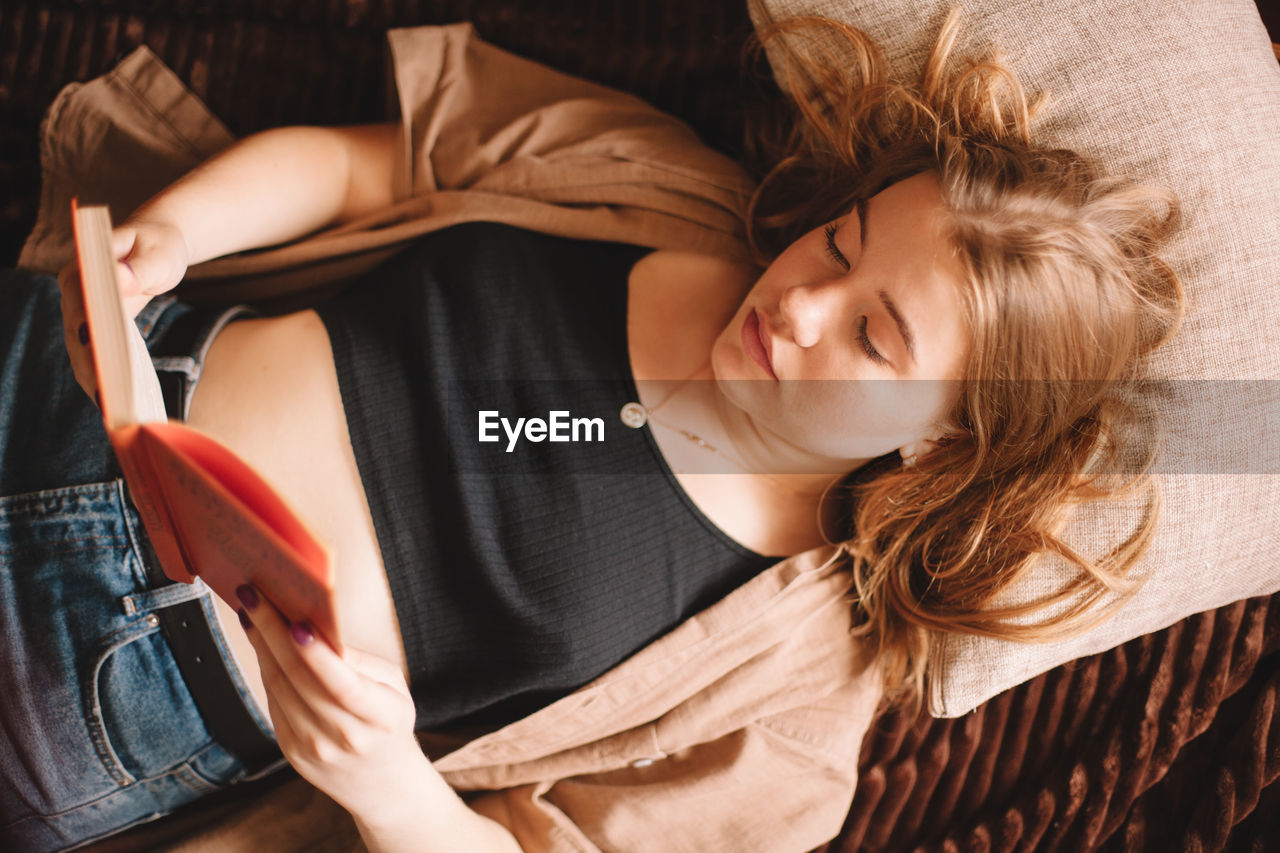 High angle view of teenage girl reading book lying on bed at home