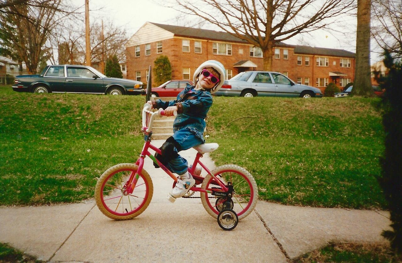 Full length portrait of smiling boy riding bicycle on footpath against house