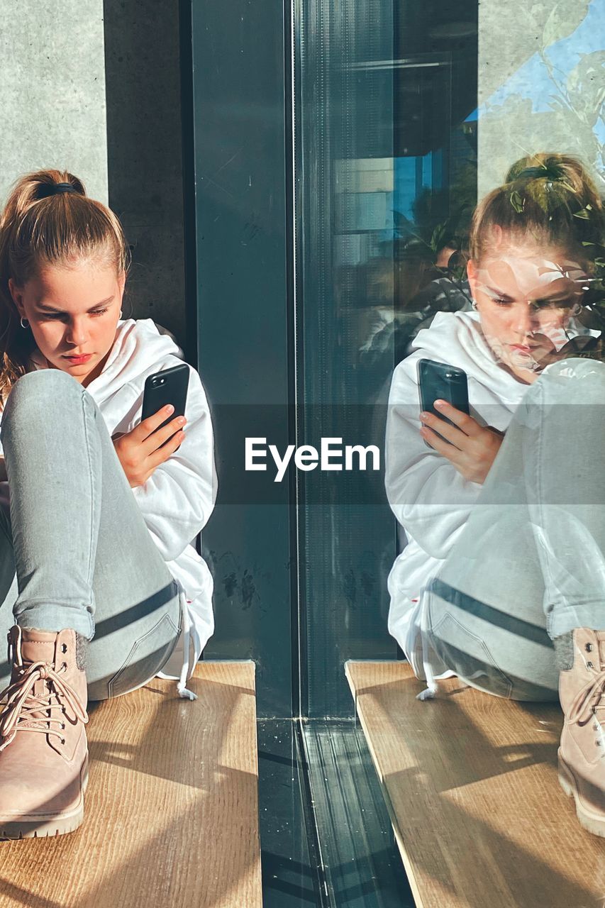  girl sitting at window using mobile phone 