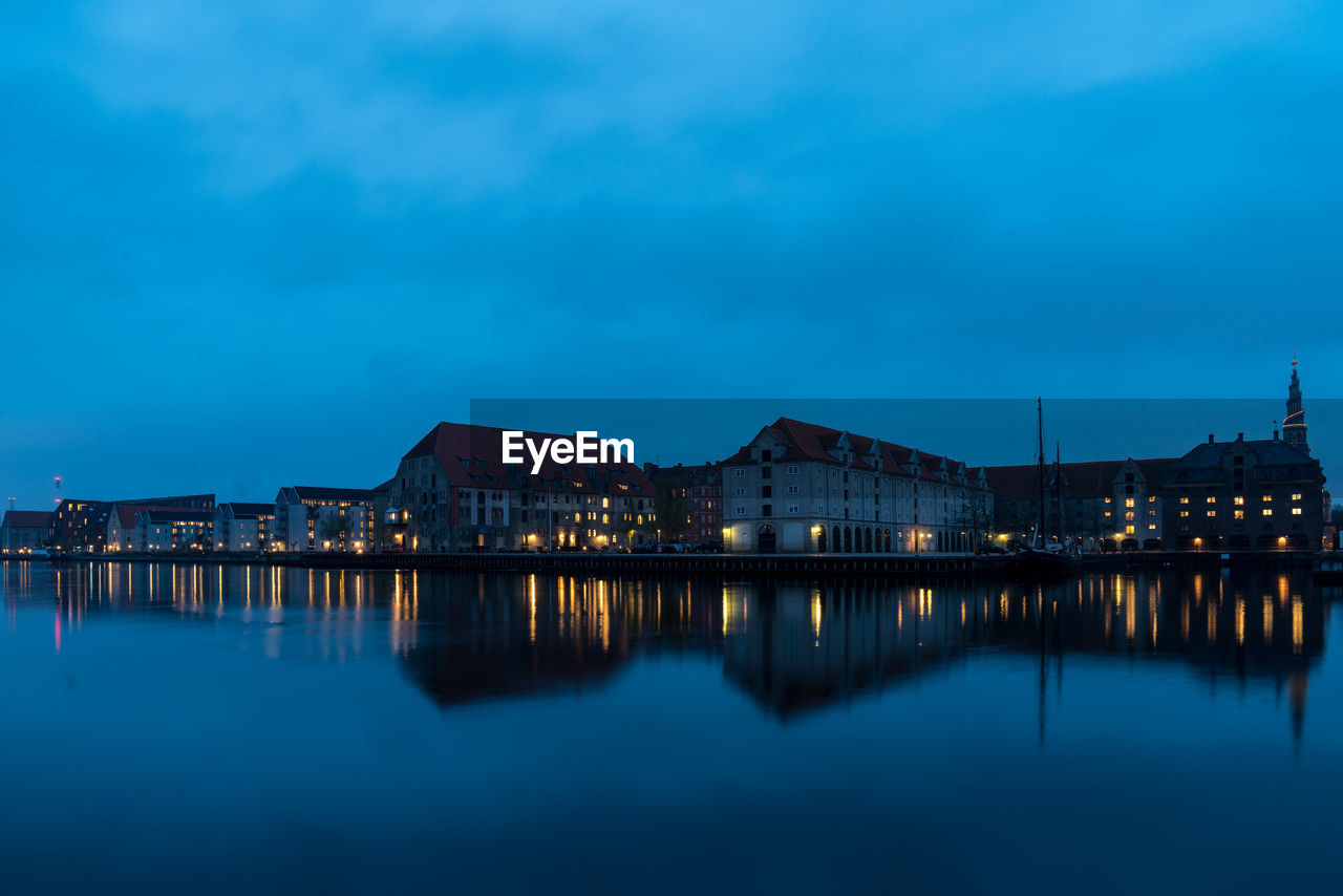 Illuminated buildings by lake against sky at night