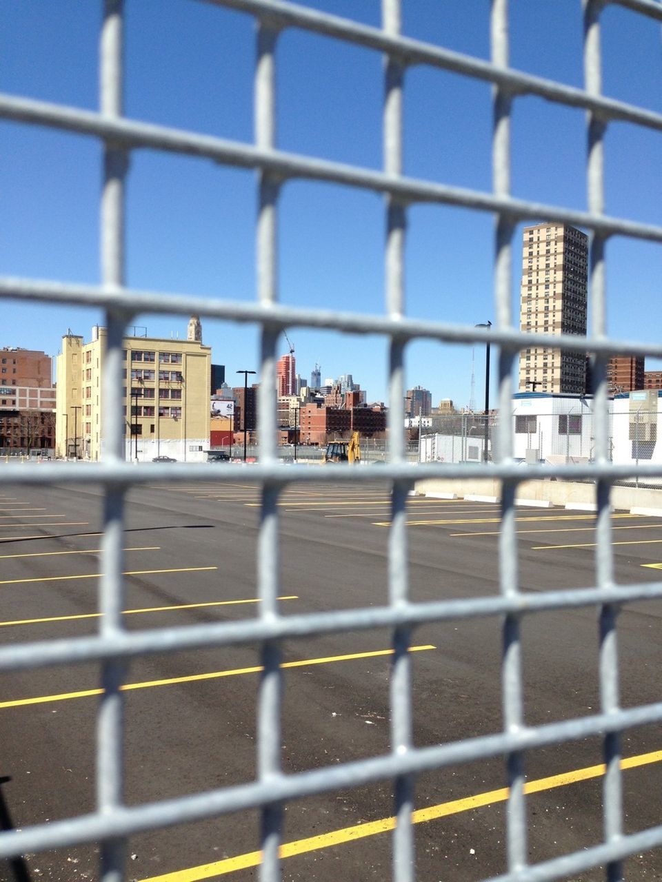 View through fence of street and buildings against blue sky