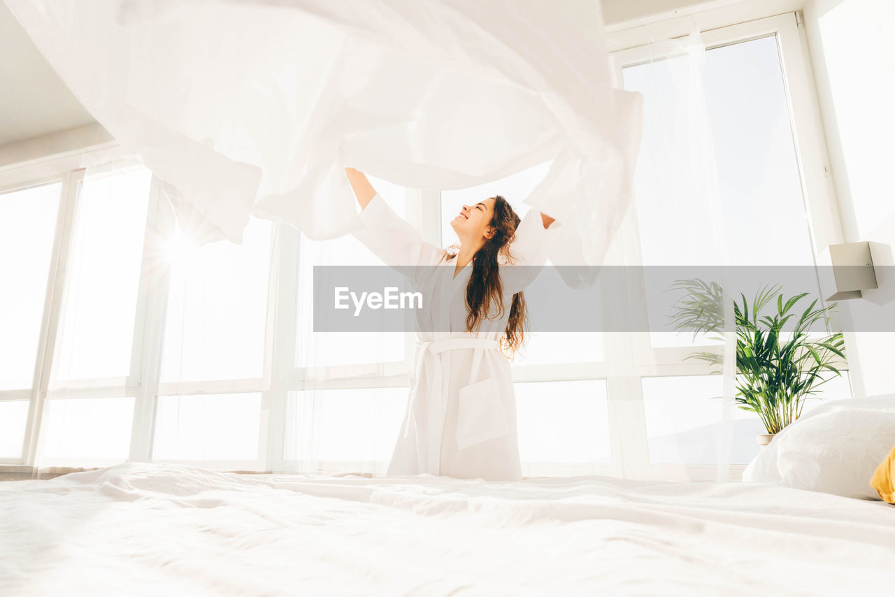Cheerful woman holding sheet at bedroom
