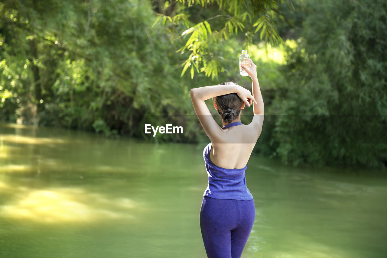 Rear view of woman standing by lake against trees