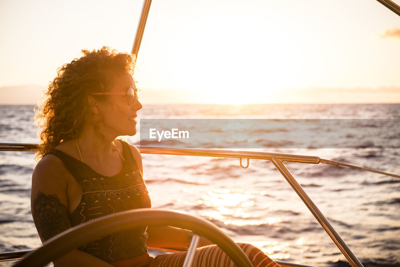 WOMAN SITTING ON BOAT AT SEA AGAINST SKY