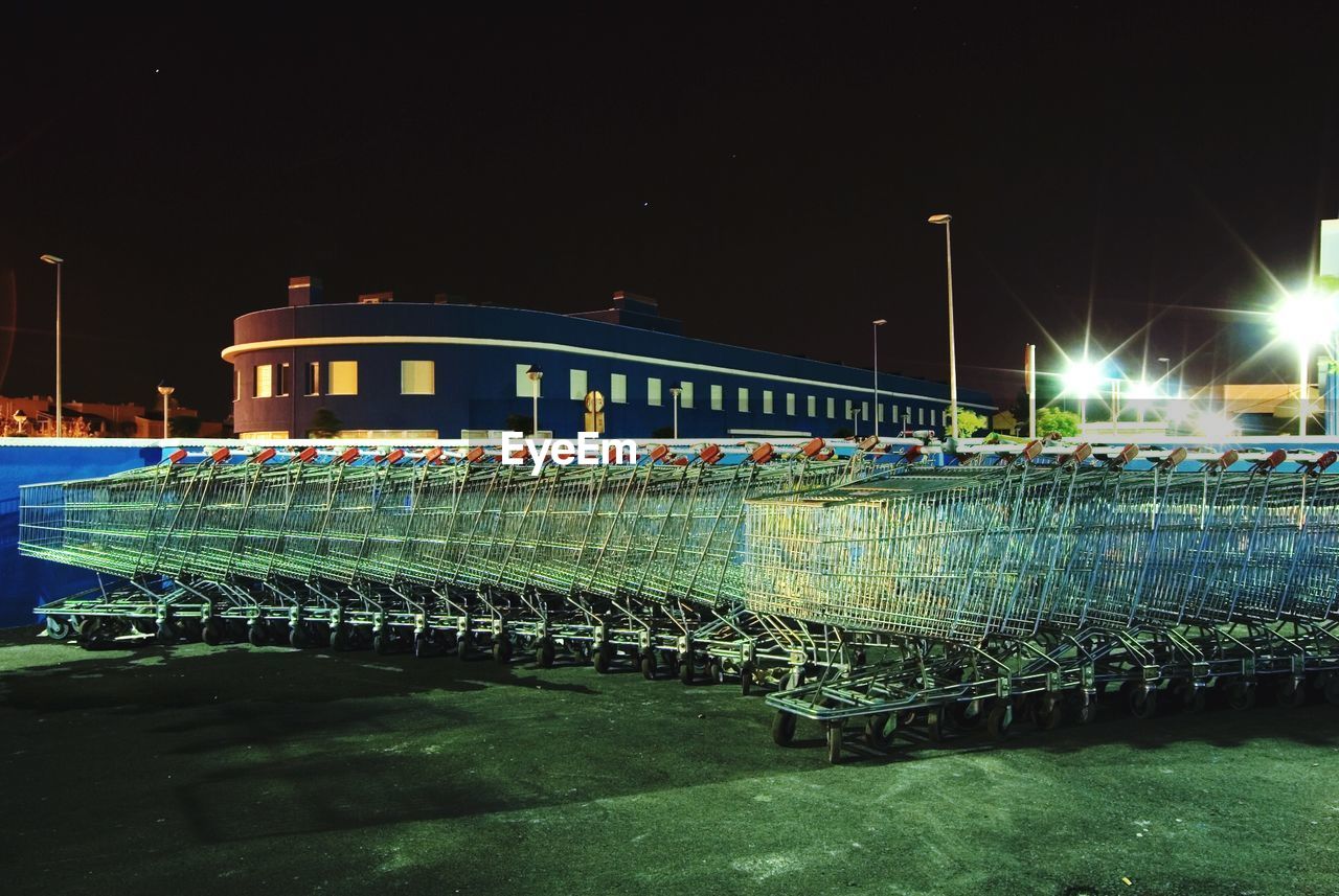 Shopping carts on field by building against sky at night