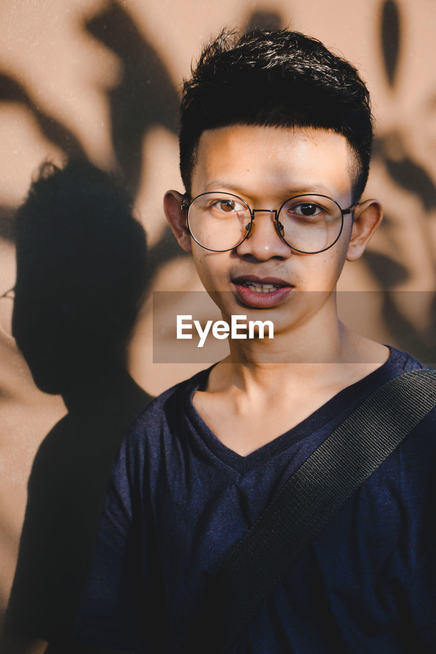 Portrait of smiling young man wearing eyeglasses against wall