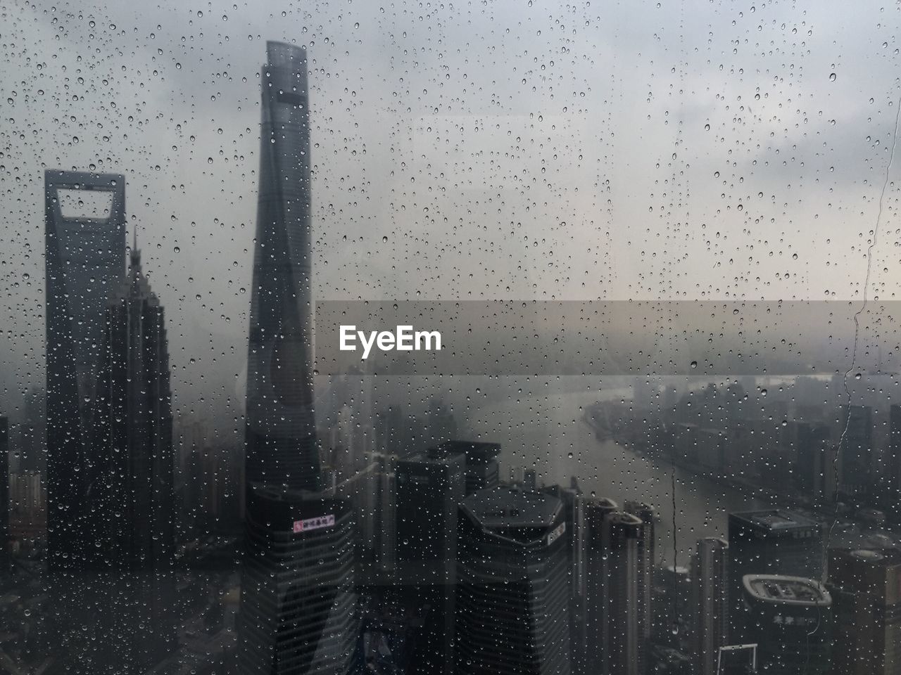 Buildings in city seen through wet window during rainy season