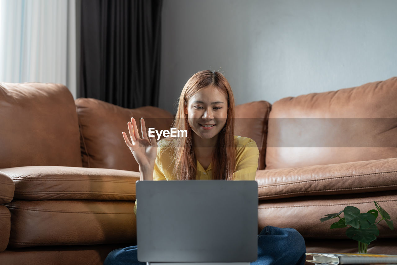 young woman using laptop while sitting on sofa at home