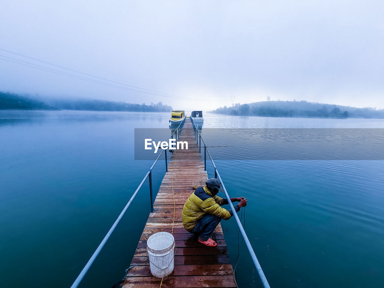 REAR VIEW OF MAN SITTING ON LAKE