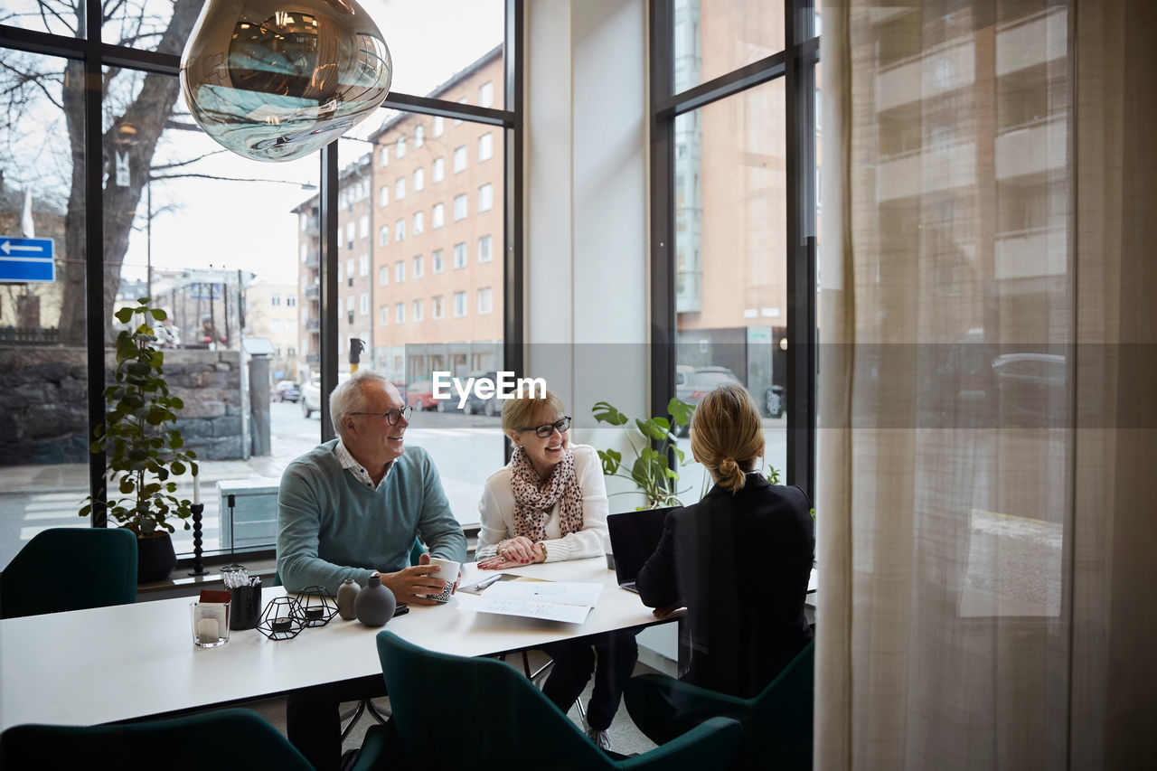 Smiling senior couple discussing with female realtor in estate office