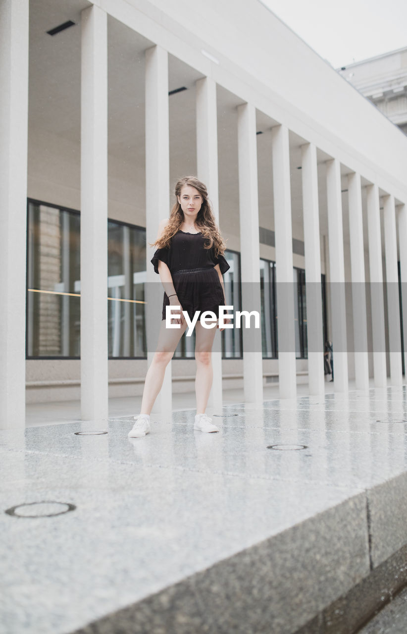 Portrait of young woman standing against building