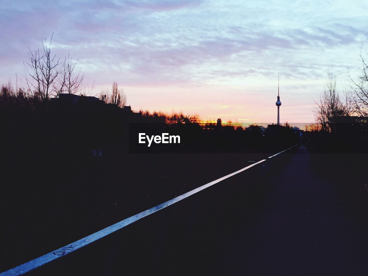 Road leading towards fernsehturm against cloudy sky during sunset