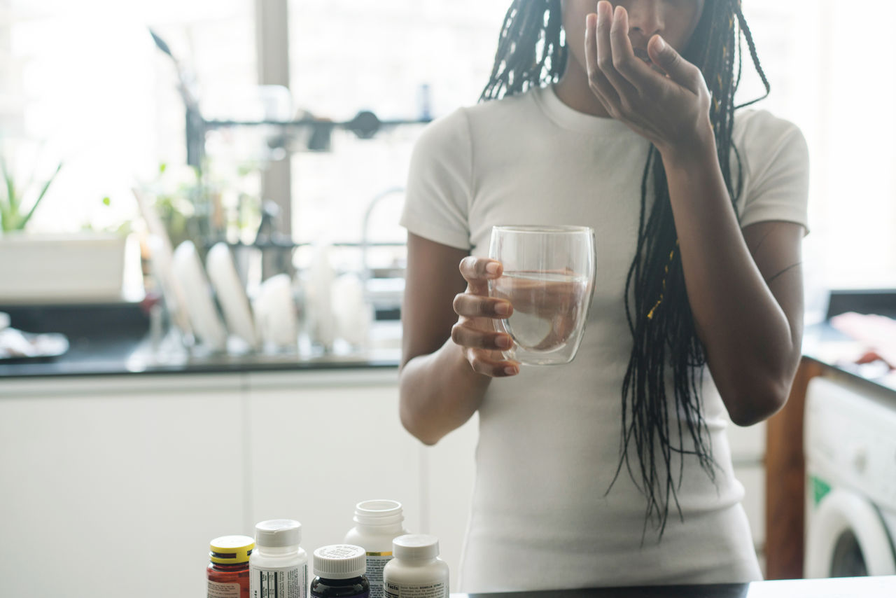 African american woman taking vitamins and supplements at home in her kitchen