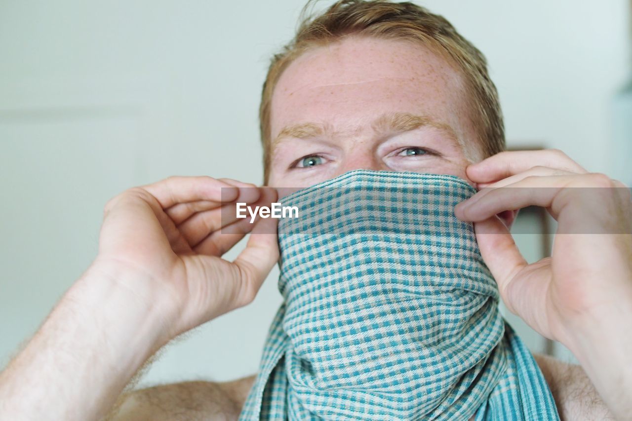 Close-up portrait of man covering face with napkin at home