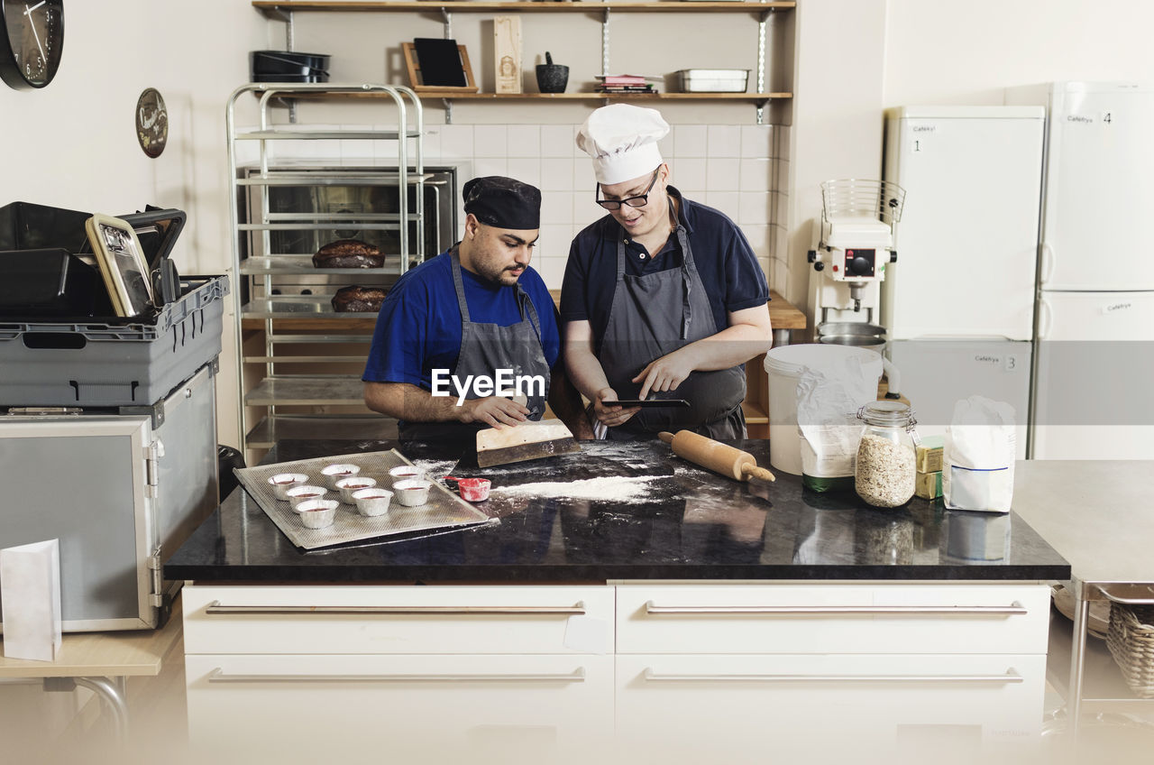 Young man showing digital tablet to coworker while cooking in kitchen