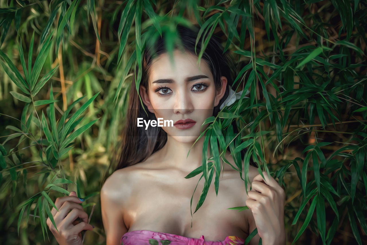 Portrait of beautiful young woman standing against tree