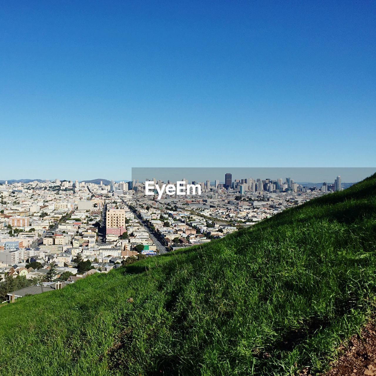 Grassy hill and cityscape against clear blue sky