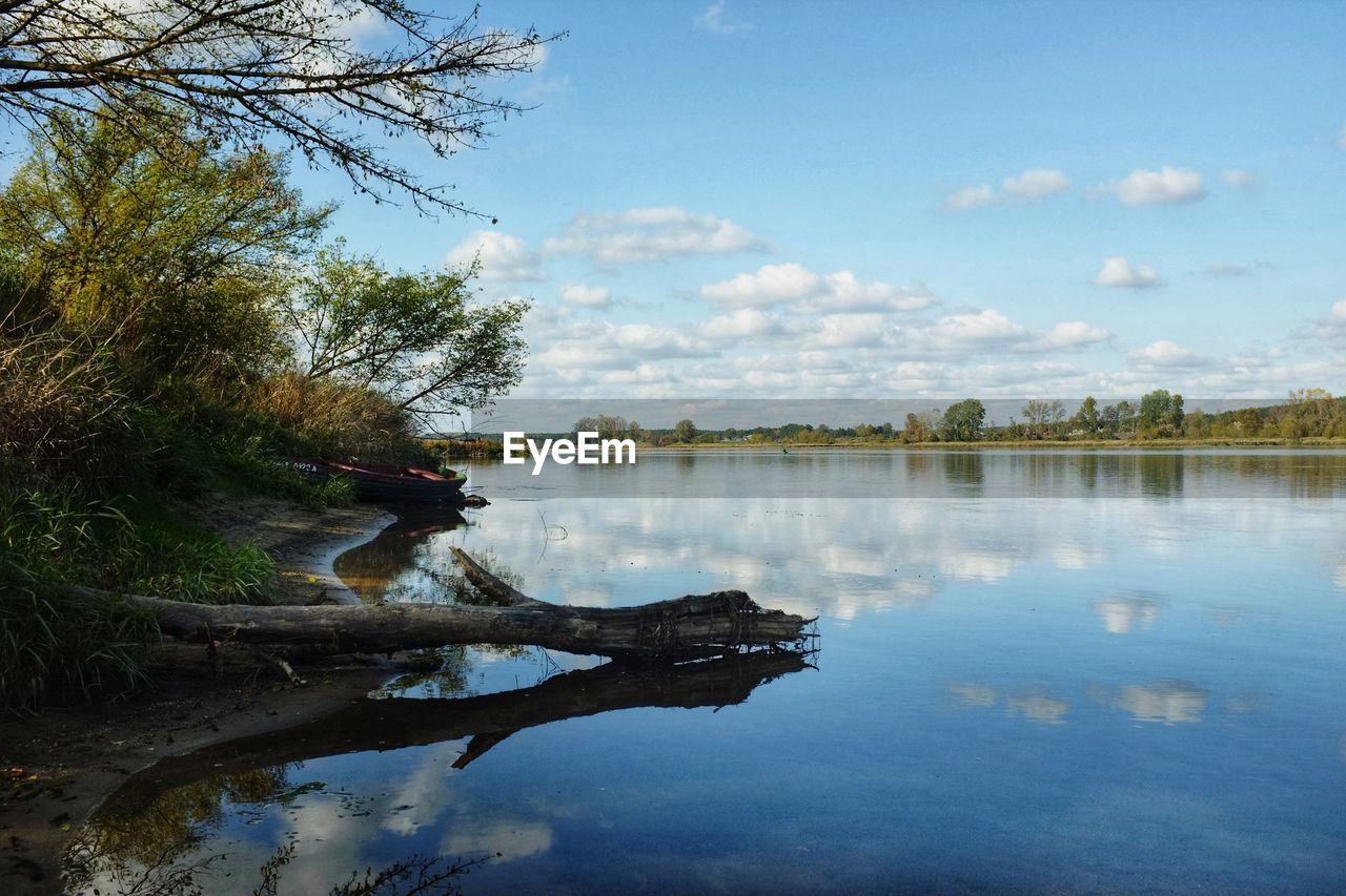 reflection, water, nature, tree, river, sky, plant, body of water, beauty in nature, tranquility, cloud, scenics - nature, tranquil scene, day, morning, one person, outdoors, landscape, non-urban scene, shore, autumn, environment, leisure activity, blue, land, men, sunlight, leaf, reservoir, travel destinations, idyllic, adult, forest, travel, full length