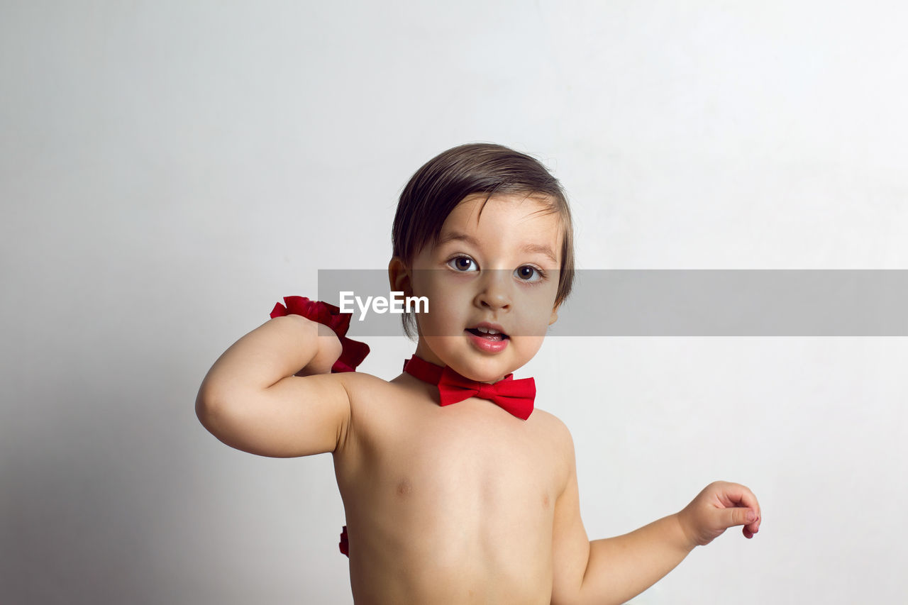 Child without a t-shirt sitting on a white background with a red bow tie